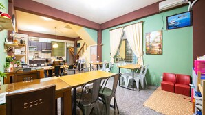 Un espace repas avec des tables et des chaises, une cuisine à l’arrière-plan et un téléviseur accroché au mur.