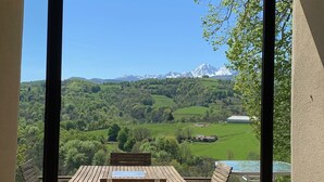 Ein Balkon mit einem Holztisch und -stühlen, der Blick auf eine grüne Landschaft und ferne Berge gewährt.
