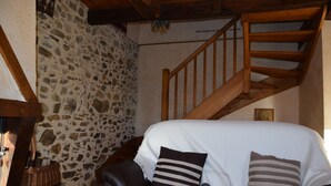 Ein gemütliches Zimmer mit Steinwand, einer Holztreppe, einem schwarzen Ledersofa und einem weißen Bett mit gestreiften Kissen.