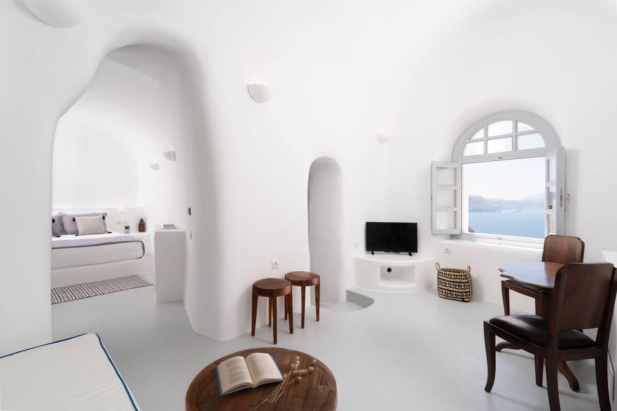 Ein modernes, minimalistisches Wohnzimmer mit großem Fenster, einem Flachbildfernseher, Holzmöbeln und einer gemütlichen Leseecke.