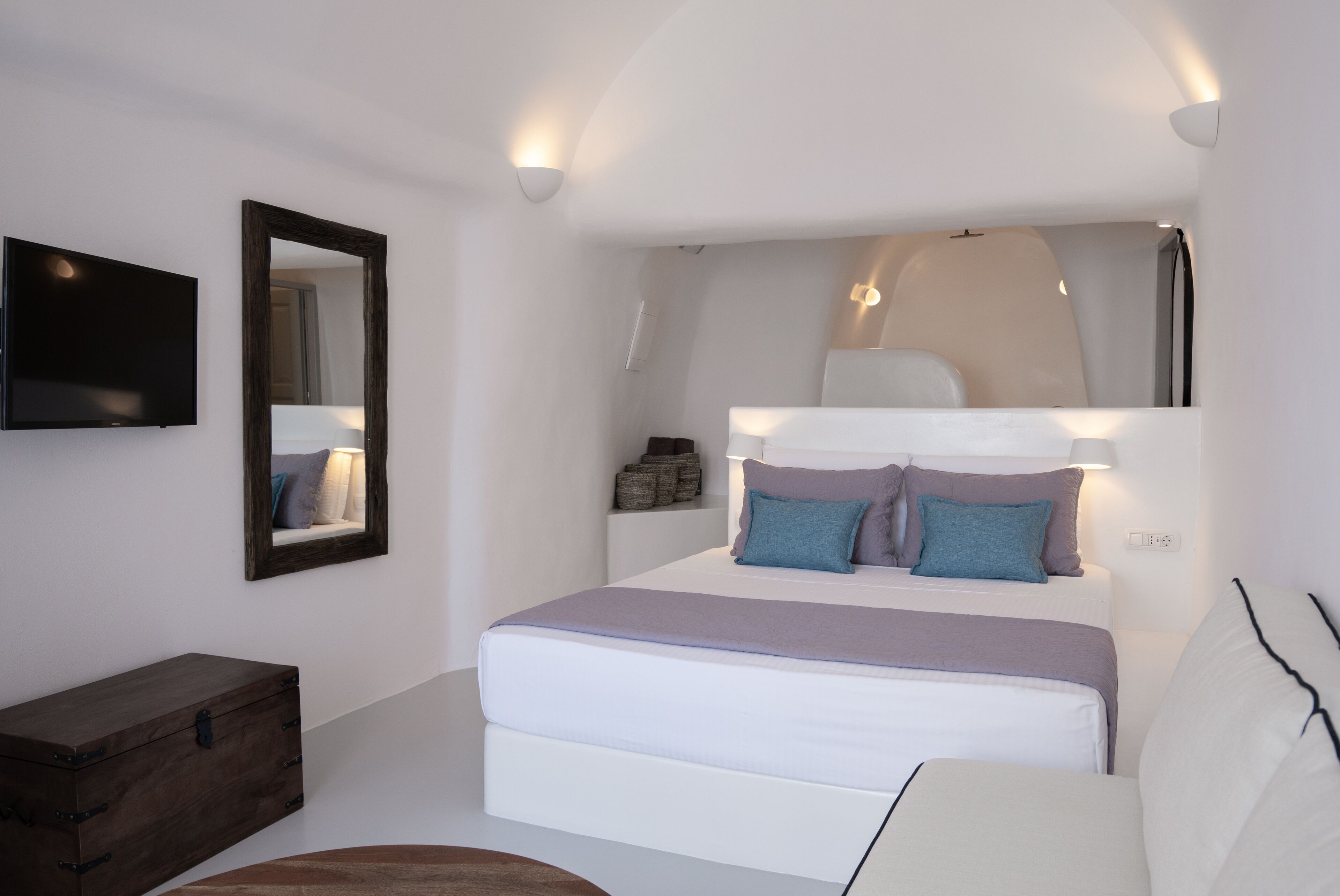 A bedroom with a large bed, a dresser, a television, and a mirror.