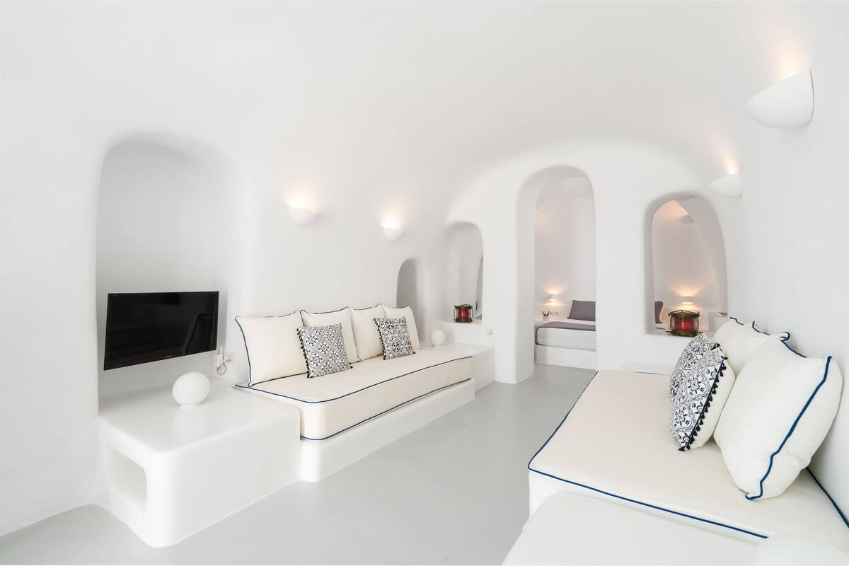 Ein modernes, minimalistisches Wohnzimmer mit weißen Sofas, einem Flachbildfernseher und integrierter Beleuchtung.