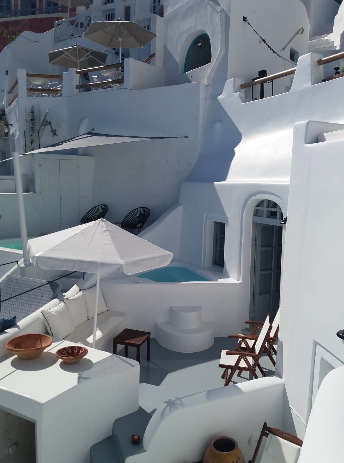 Un espacio exterior moderno y luminoso con jacuzzi, sillones de descanso y sombrillas.