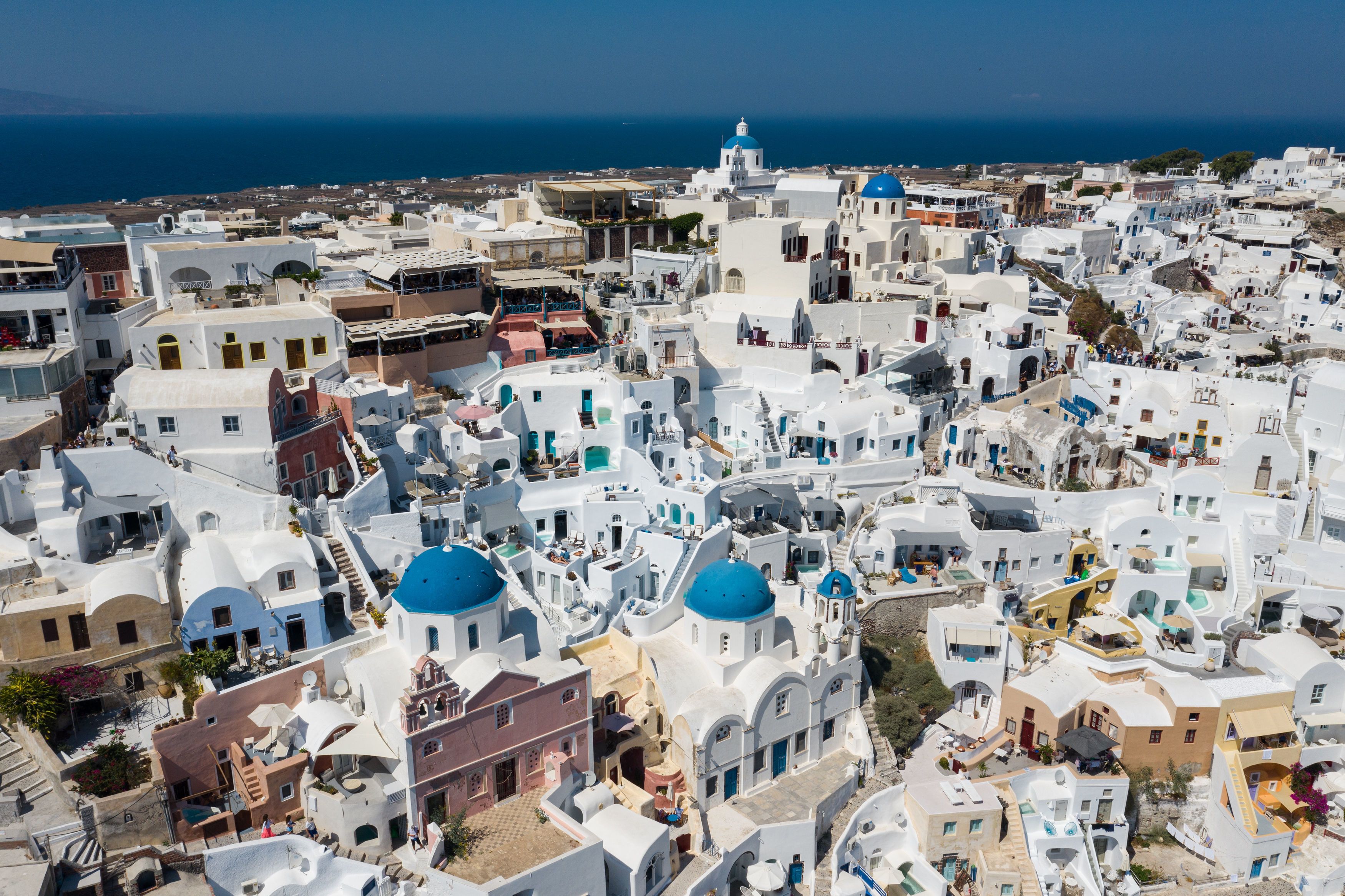A densely packed coastal town with white buildings and blue domed roofs, likely a tourist destination.