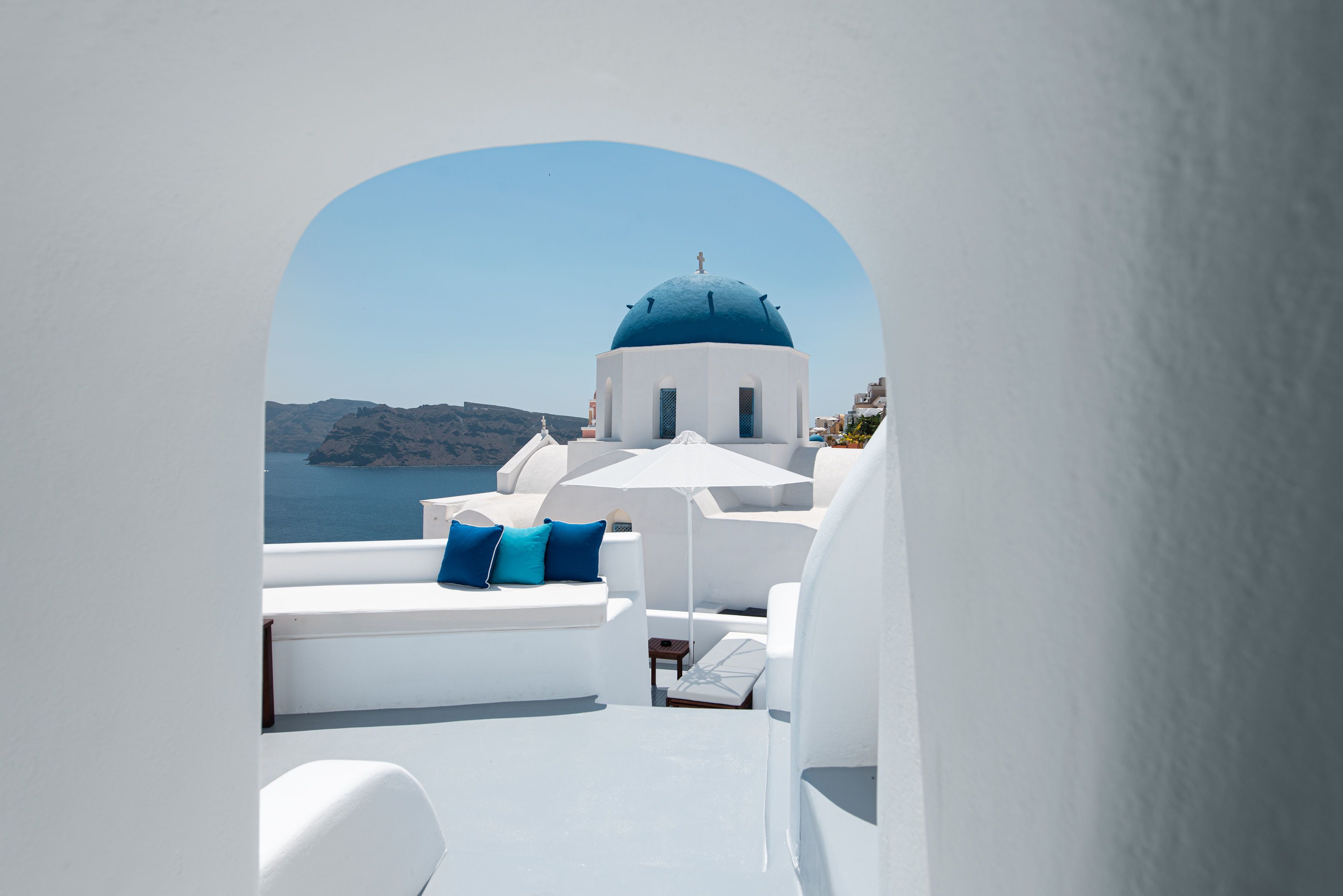 Un edificio blanco con una cúpula azul, muebles blancos y vista al mar.
