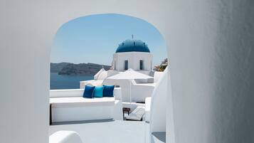 Un edificio blanco con una cúpula azul, muebles blancos y vista al mar.