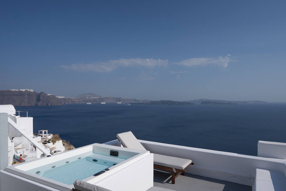 Eine Dachterrasse mit Whirlpool, weißen Möbeln und Blick auf das Meer und vorgelagerte Inseln.