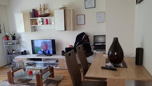 Un salon moderne avec une table basse en verre, un téléviseur et un coin repas comprenant une table et des chaises en bois.