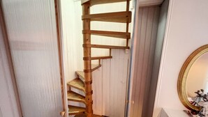 A wooden spiral staircase in a hallway with white walls and a mirror on the right.