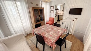A dining area with a table set for four, a wooden cabinet with glass doors, a red chair, and a white crib.