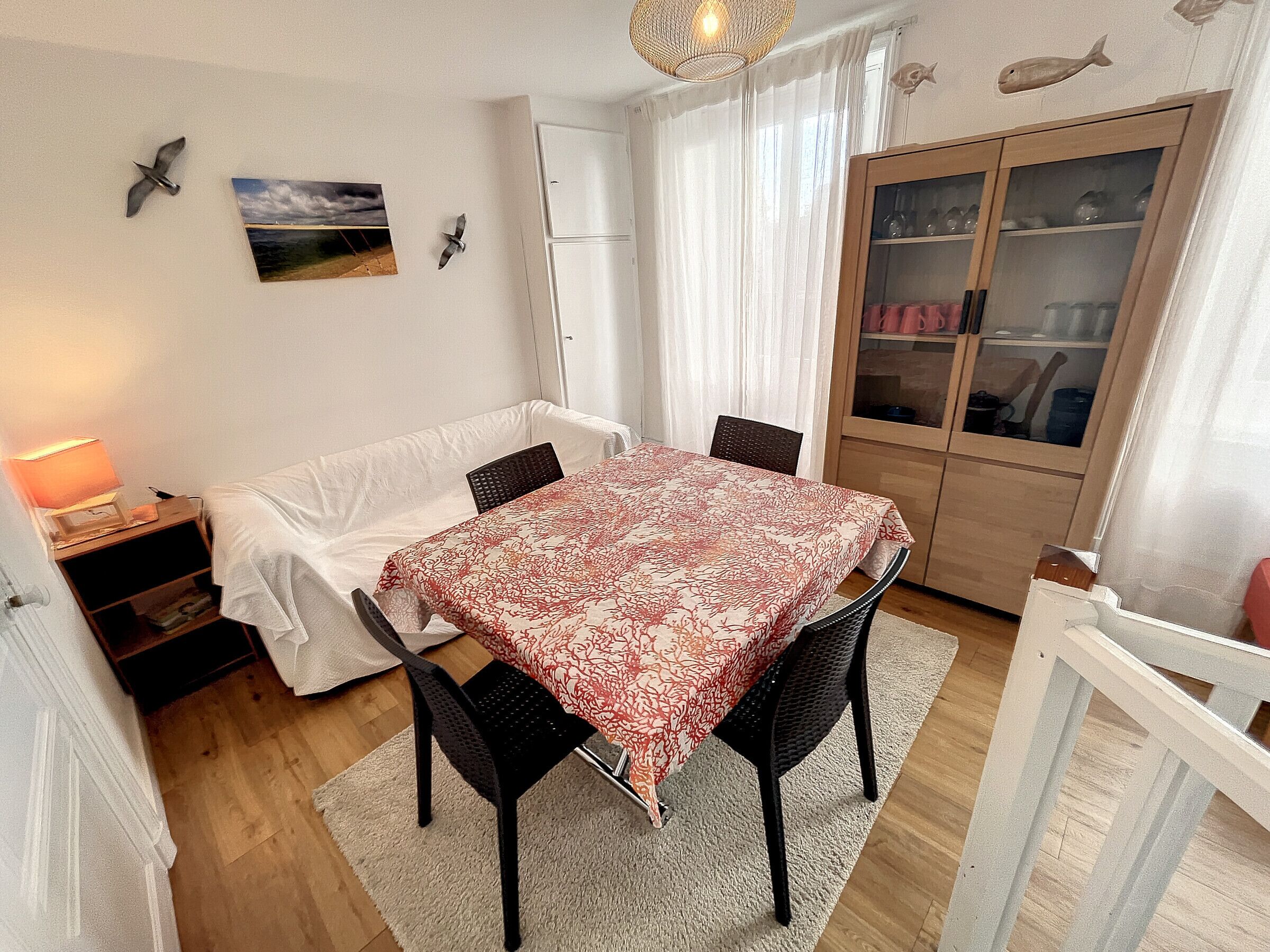 A dining area with a table covered by a patterned tablecloth, surrounded by chairs.