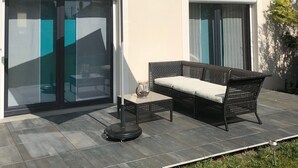 Un patio con un paraguas azul, un sofá de mimbre y una mesa con una vela.