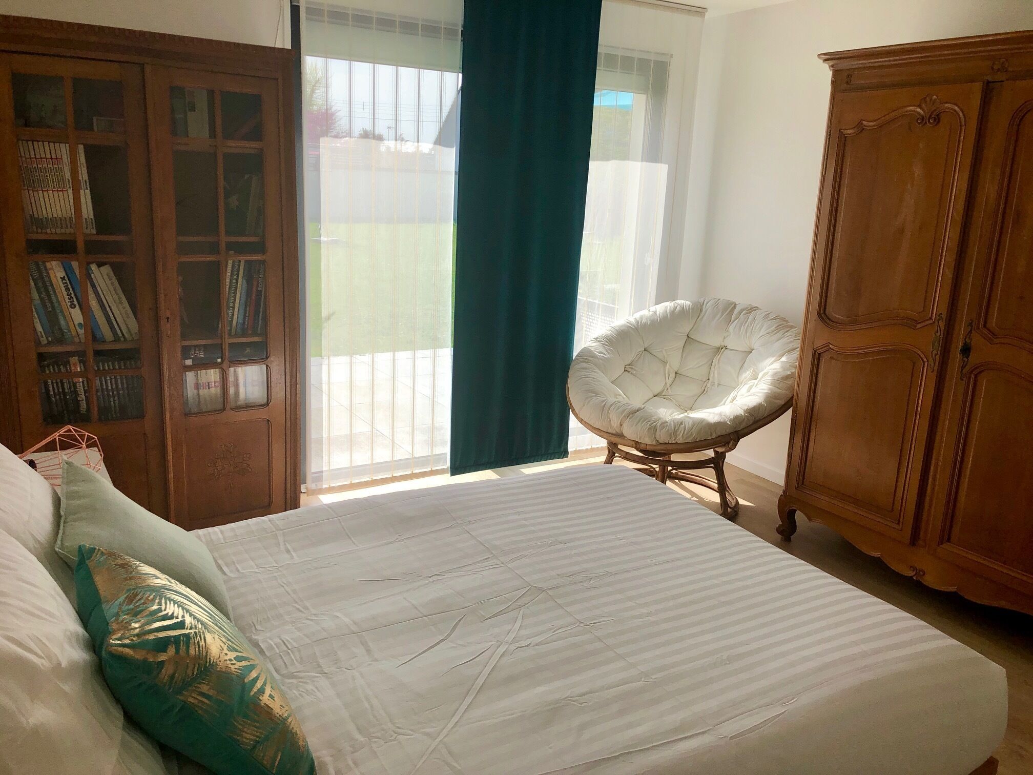 A bedroom with a bed, a chair, a wardrobe, and a window with curtains.