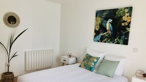 Un dormitorio con una cama grande, una mesita de noche, un radiador, una planta en maceta y un cuadro colgado en la pared.