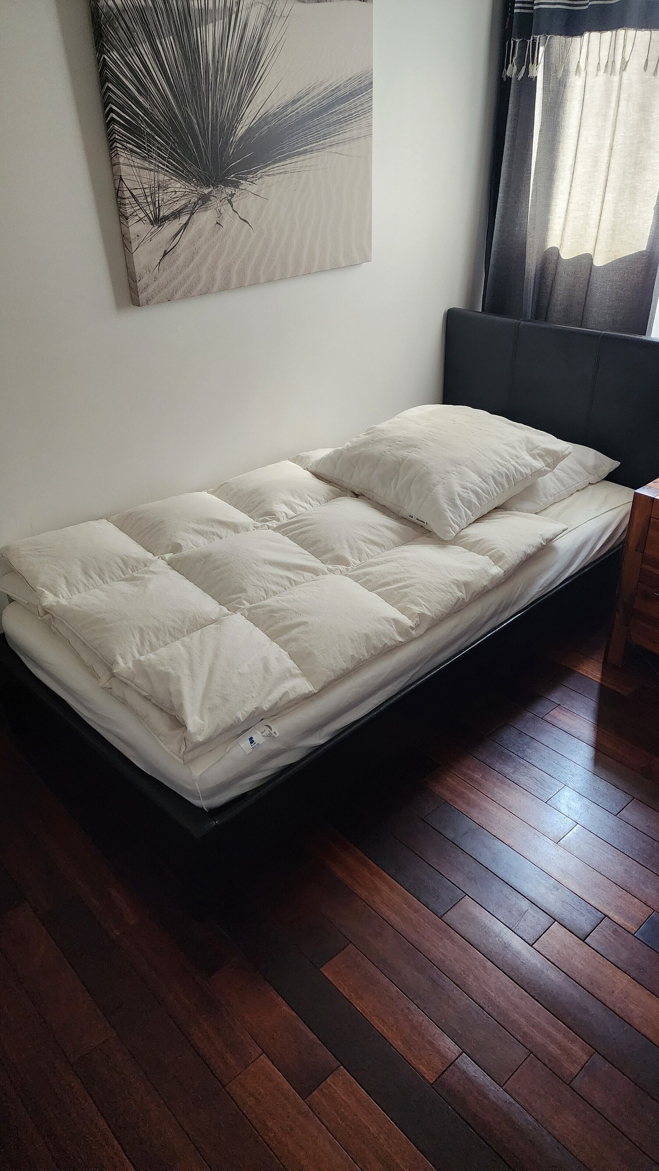Un lit avec une tête de lit, un plancher en bois et un mur orné d’une œuvre d’art abstraite.