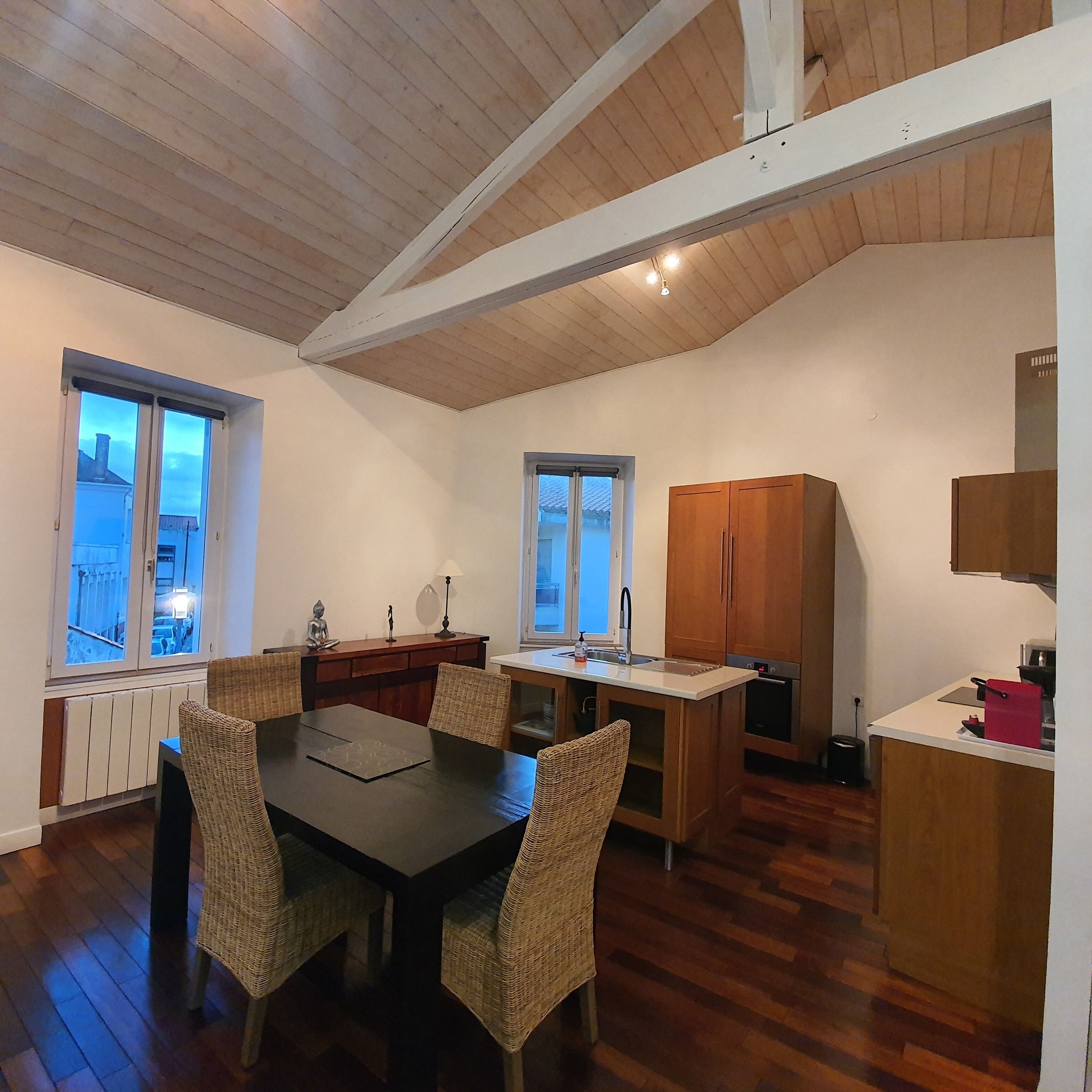 Une cuisine de taille réduite, dotée de meubles en bois, une table à manger avec des chaises, et une vue agréable par les fenêtres.