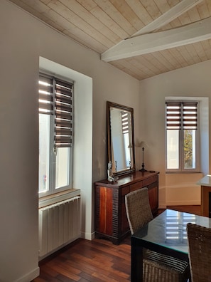 Una habitación con pisos de madera, una mesa de comedor con sillas, un aparador y dos ventanas con persianas.