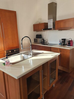 Una cocina moderna con armarios de madera, un lavamanos de acero inoxidable, un microondas, un tostador y una cafetera.