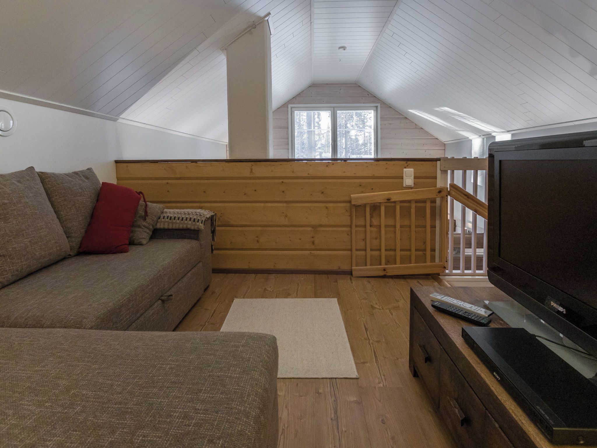 A cozy living room with a sofa, a television, and a wooden floor.