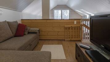 A cozy living room with a sofa, a television, and a wooden floor.