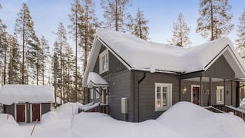A cabin with a snow-covered roof, surrounded by tall trees.