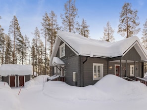 A cabin with a snow-covered roof, surrounded by tall trees. - Vanamotupa by Interhome (Äkäslompolo)