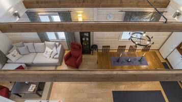 A spacious loft-style living area with a high ceiling, a red armchair, a sofa, and a dining table with chairs.