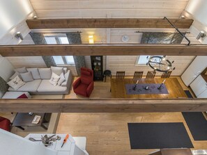 Amplio espacio tipo loft con techos altos, un sillón rojo, un sofá y una mesa de comedor con sillas.