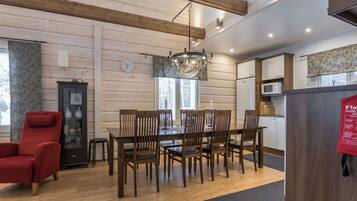 A cozy dining area with wooden chairs and a table, a red armchair, a cabinet with glass doors, and a chandelier.