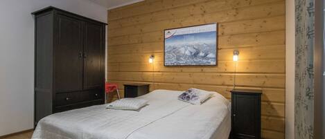 A bedroom with a wooden headboard, a bed with white bedding, two bedside tables, and a nightstand.