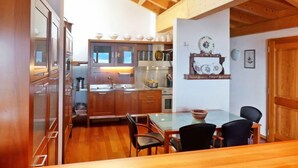 A modern kitchen with wooden cabinets, a glass dining table, and a wooden ceiling. - Sunset B 11 by Interhome (Villars)