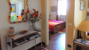 Una habitación con una cama, una mesita de noche con libros, un espejo y un jarrón con flores.