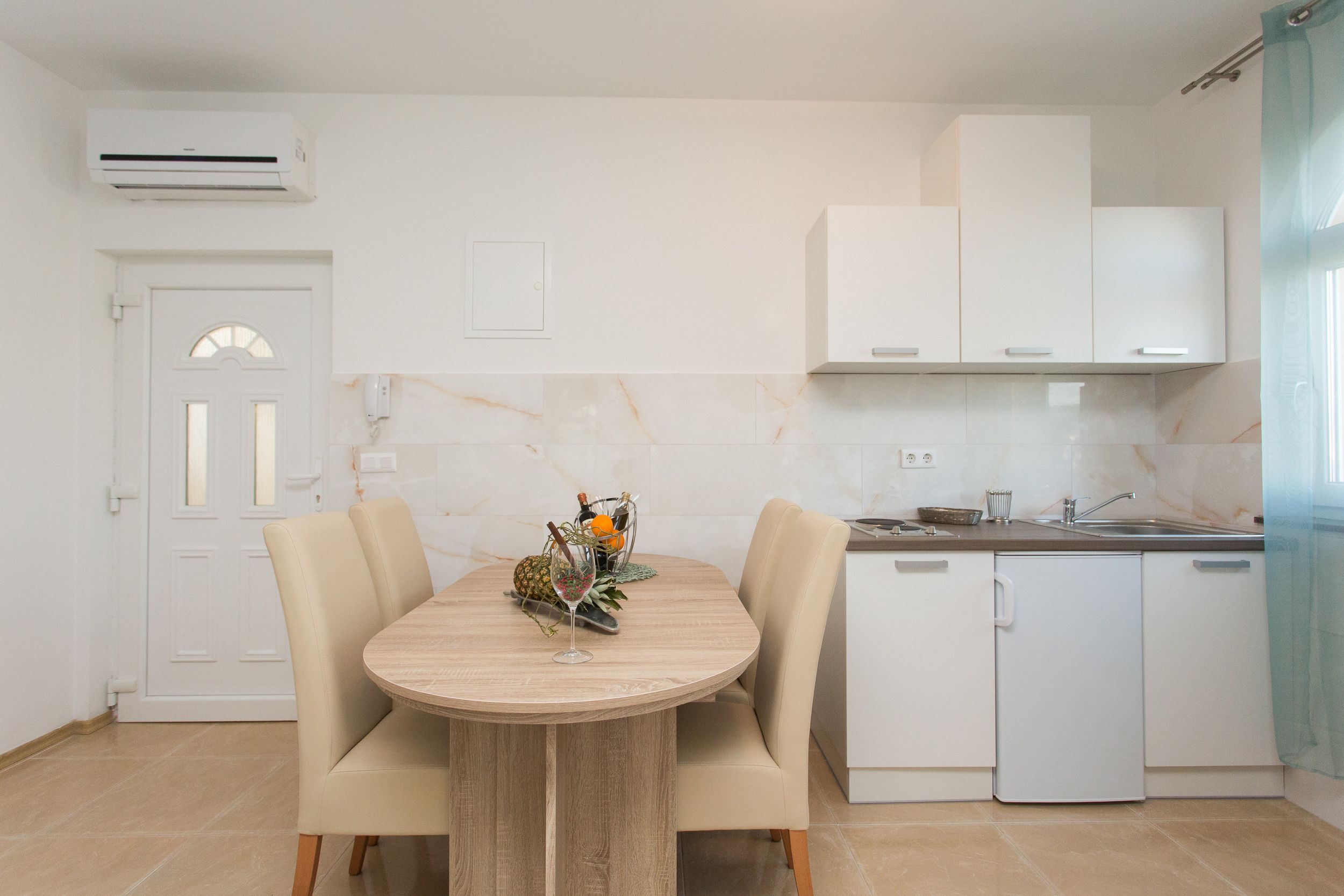 A compact kitchen with white cabinets, a built-in dishwasher, and a dining area with a wooden table and chairs.