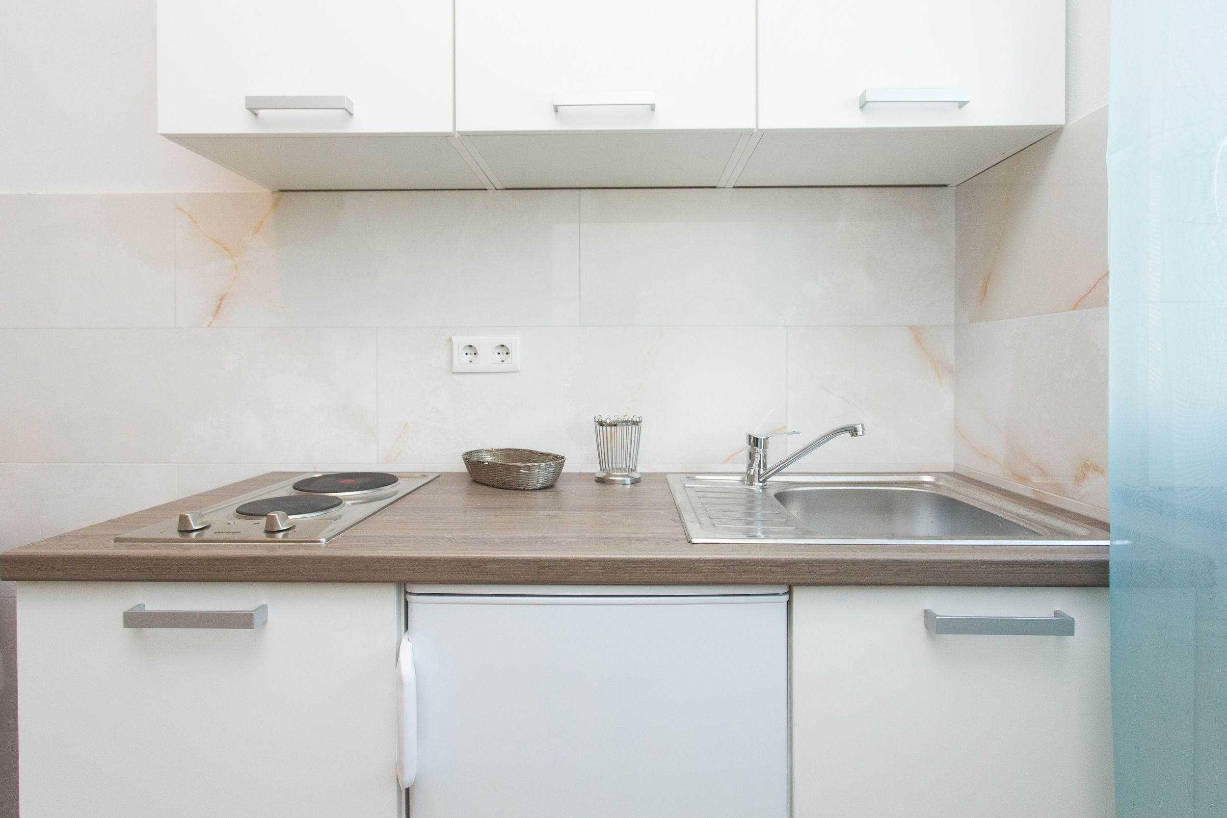 A modern kitchen with white cabinets, a wooden countertop, a sink, and a stove.