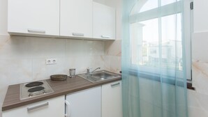 Une cuisine moderne avec des meubles blancs, un évier en acier inoxydable et une porte vitrée donnant sur un balcon.