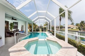 Relax by the pool surrounded by lush greenery and a serene body of water.