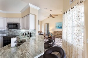 Enjoy cooking in this well-equipped kitchen with microwave and stainless steel sink, adjacent to a cozy living area with a comfortable sofa.