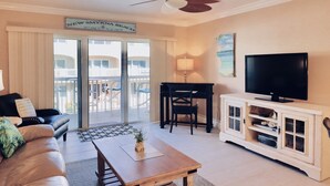 Ein Wohnzimmer mit einer Couch, einem Couchtisch, einem Fernseher und einem Balkon mit einem Schild, auf dem 'NEW SMYRNA BEACH' steht.