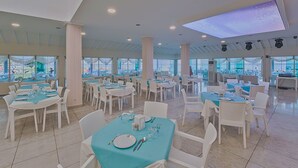 Un comedor amplio con varias mesas y sillas, ventanas grandes que ofrecen vistas de la ciudad, y un techo con iluminación empotrada y un tragaluz.