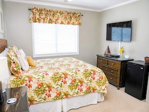 A bedroom with a bed, a dresser, a television, and a window with blinds.