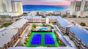 A hotel complex with multiple buildings, a tennis court, and a pool area.