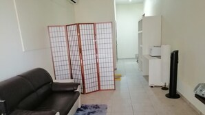 A living room with a sofa, a blue rug, a partition, a television, and a refrigerator. - D-Tas appartement en studio (Paramaribo)