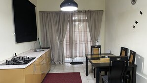 A compact kitchen with a gas stove, wooden cabinets, and a dining area with a table and chairs. - D-Tas appartement en studio (Paramaribo)