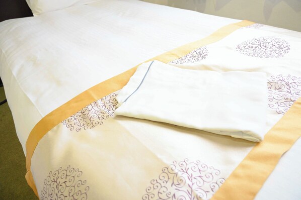 A neatly made bed with a white and gold bedspread, featuring intricate purple designs.