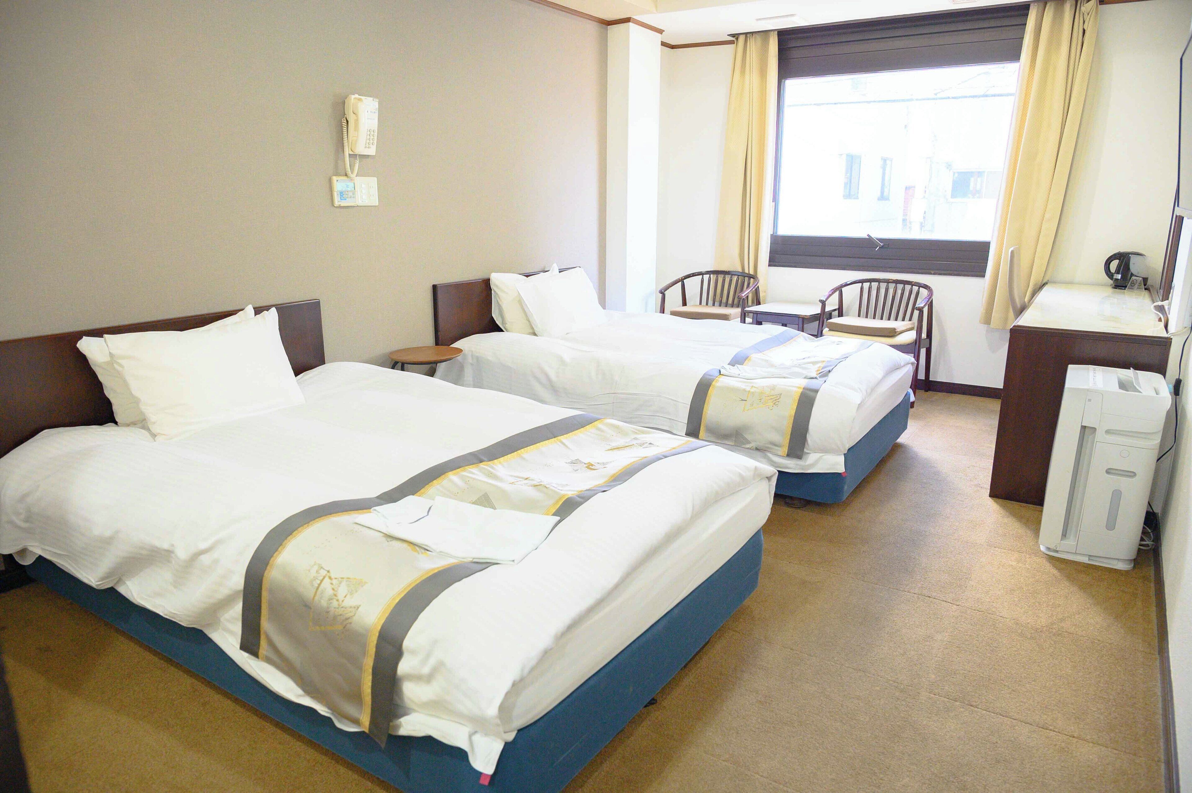 Habitación de hotel con dos camas, un escritorio, una silla y una ventana con cortinas.