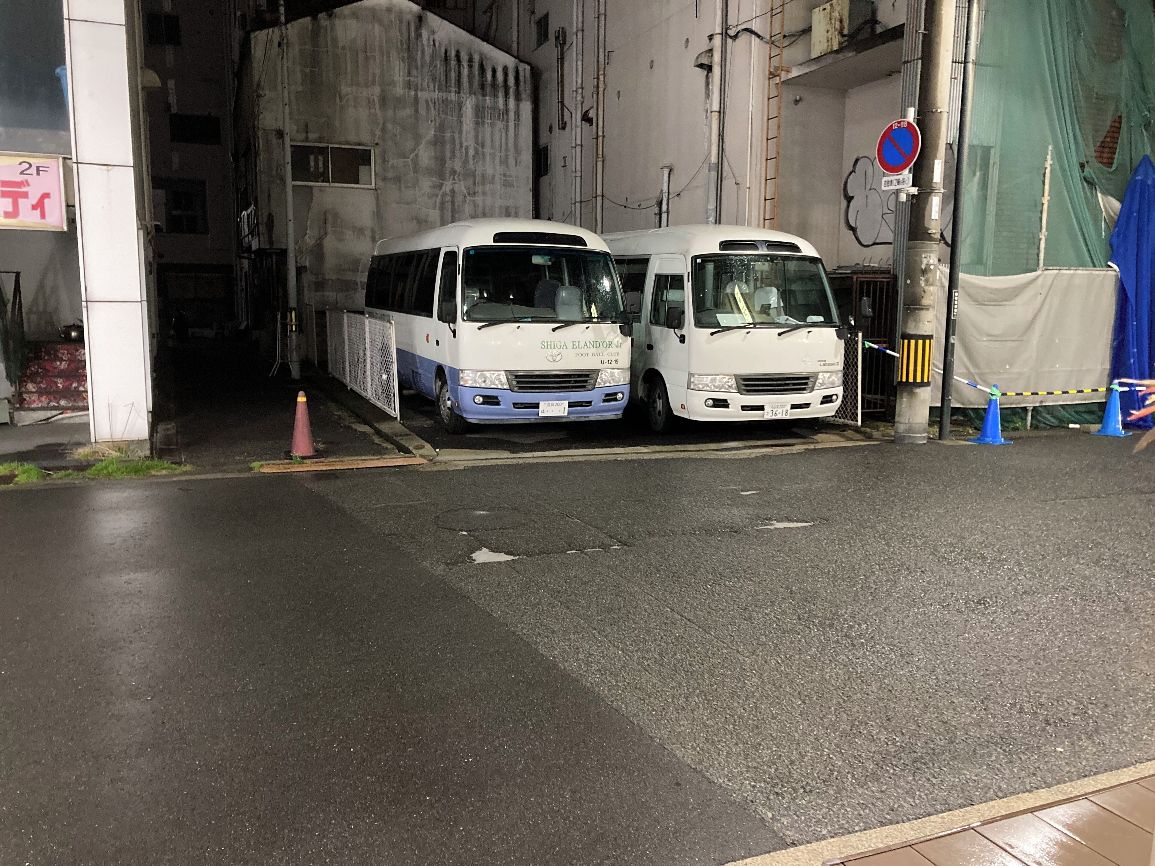 Two buses parked in a covered area with a no parking sign visible.