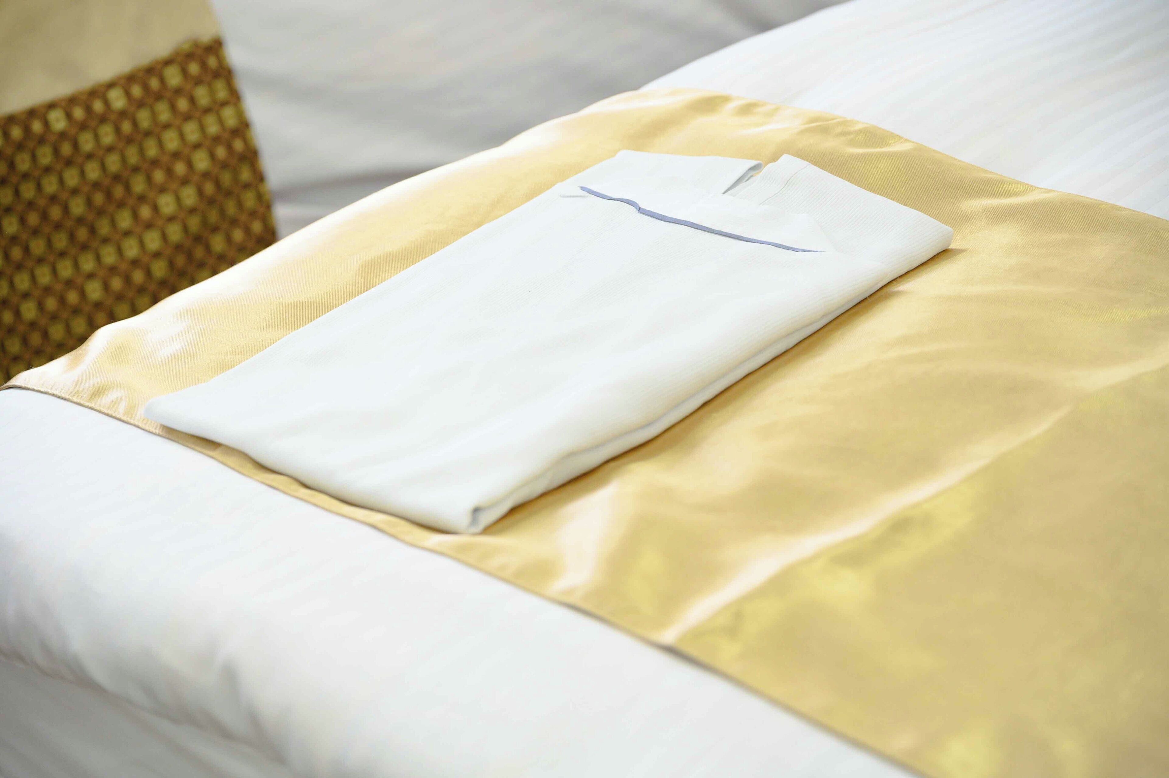 A neatly made bed with a white sheet and a folded white towel on a gold pillow.
