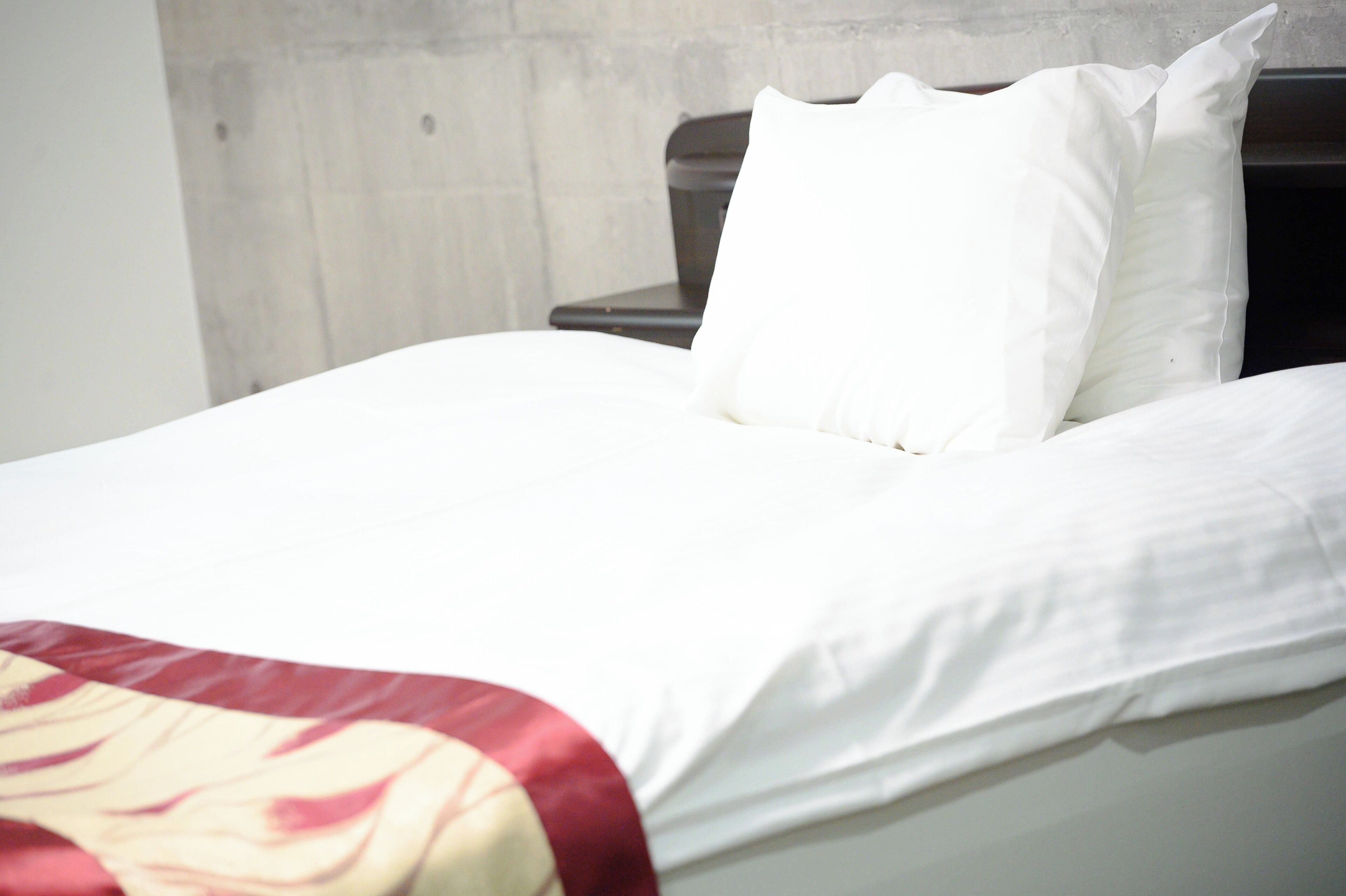 A neatly made bed with white linens and a red and beige blanket.