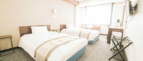 A hotel room with two beds, a small table, a chair, a desk, and a window.