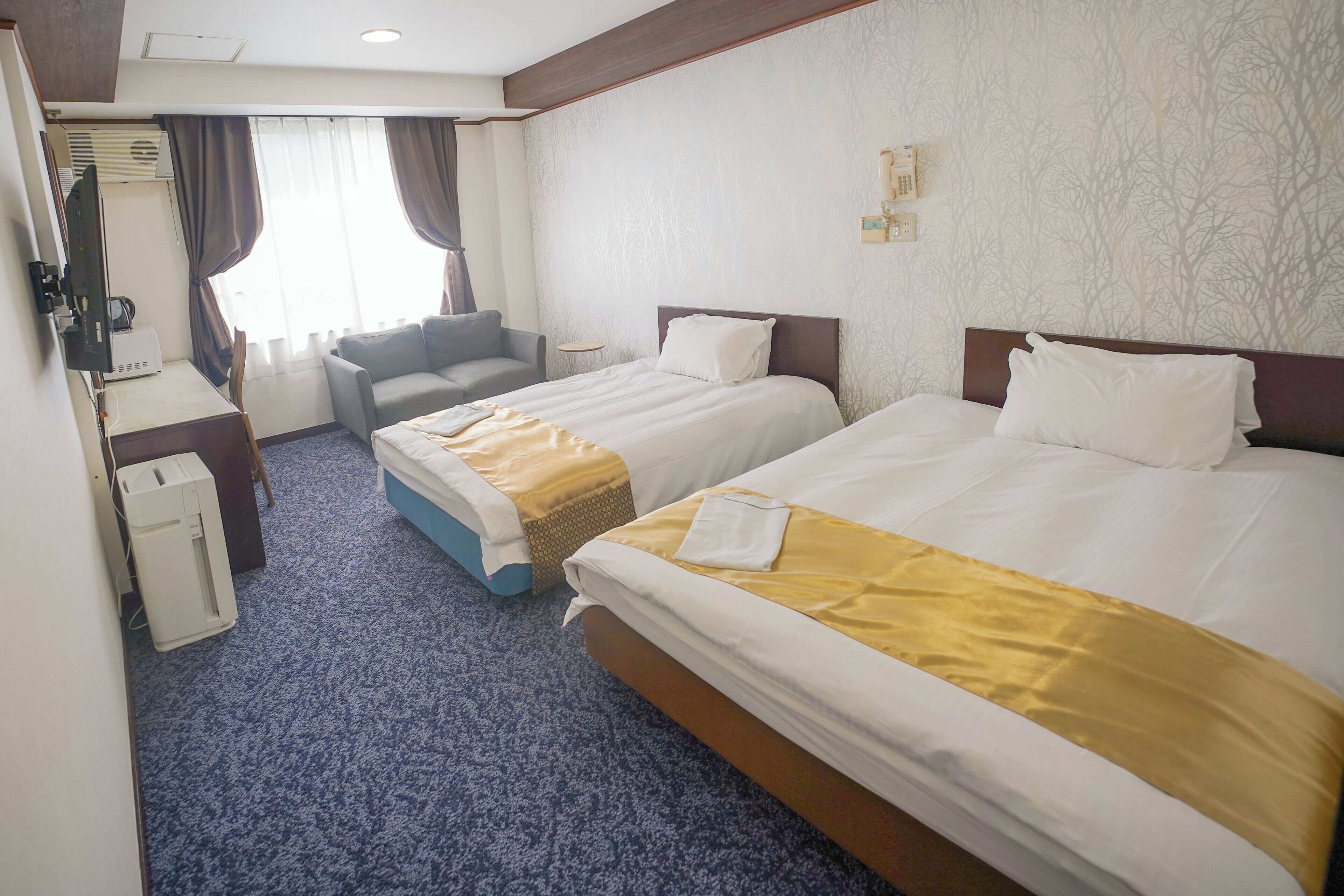 A hotel room with two beds, a desk, a chair, and a window with curtains.
